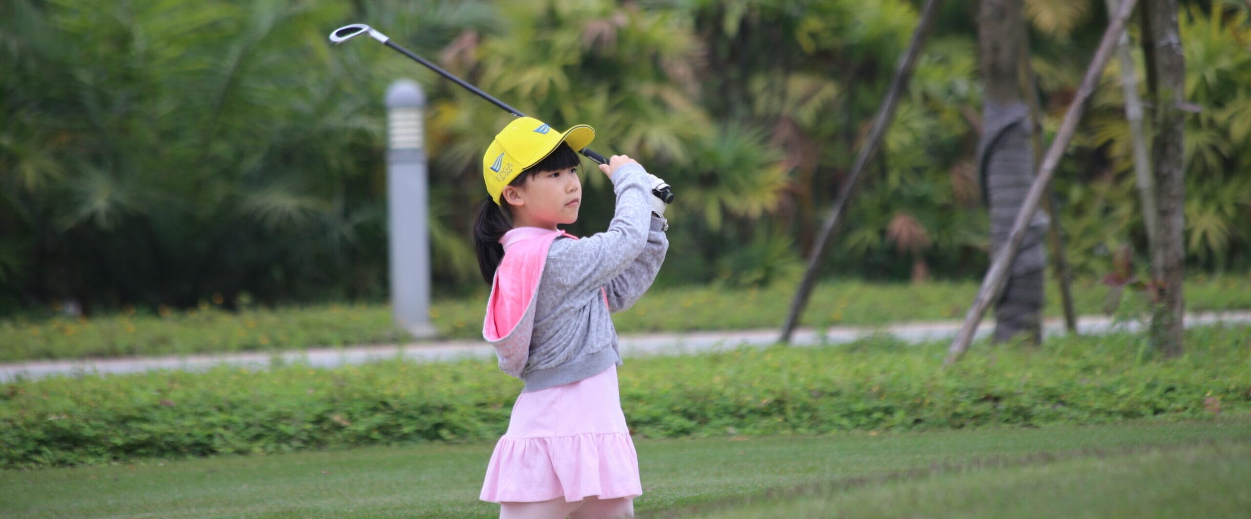 young girl swinging a golf club on grassy course