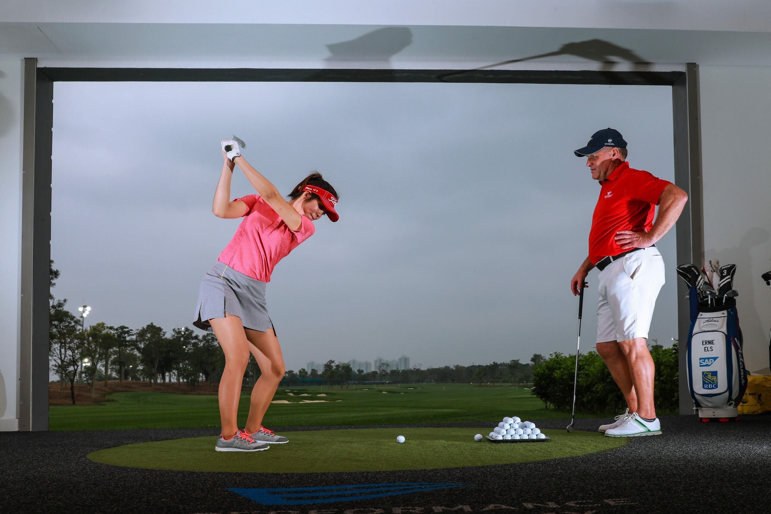 woman taking a golf swing with instructor watching over